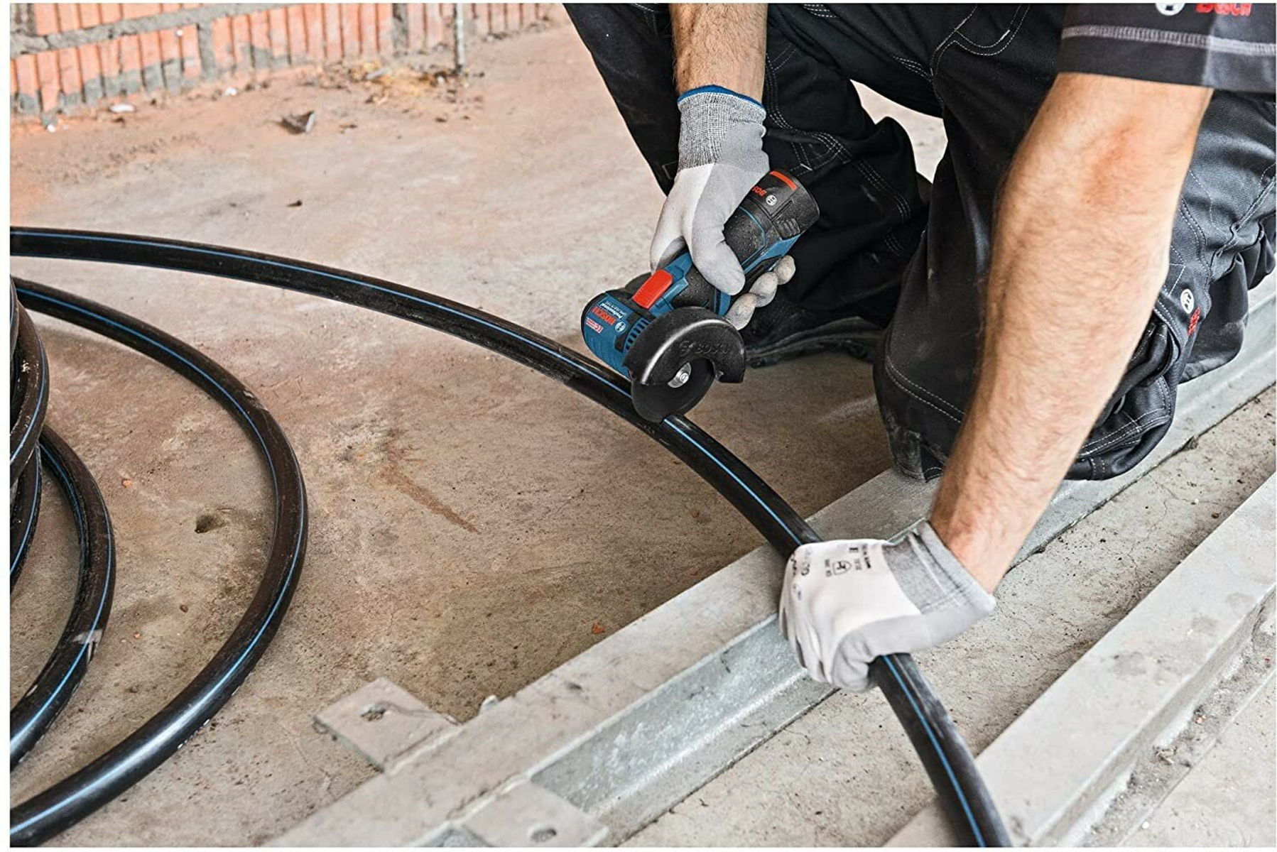 Osoba używająca szlifierki kątowej do cięcia czarnej rury na placu budowy, w rękawicach.