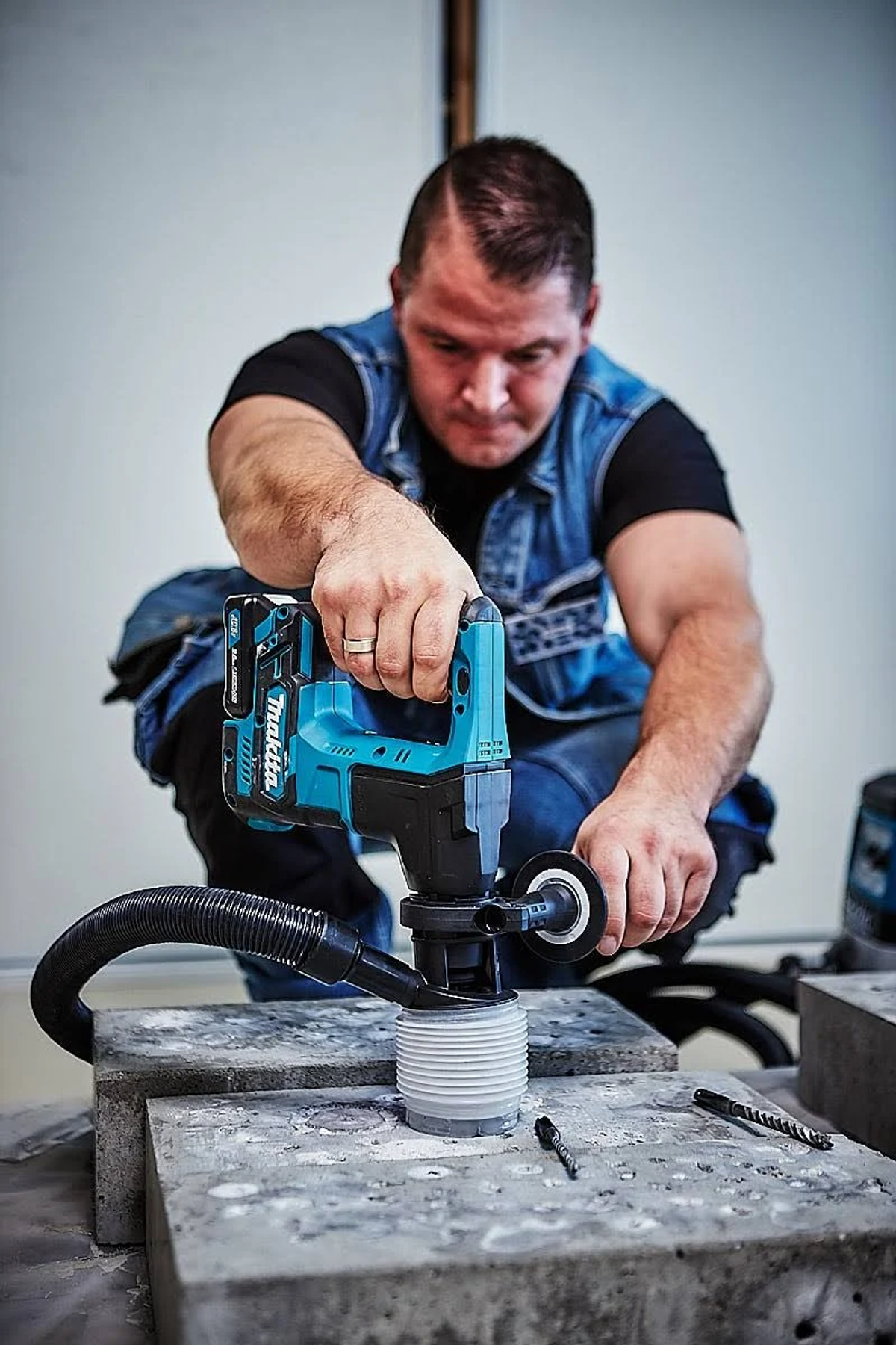Un hombre en cuclillas usando una herramienta eléctrica azul y negra con una manguera conectada.