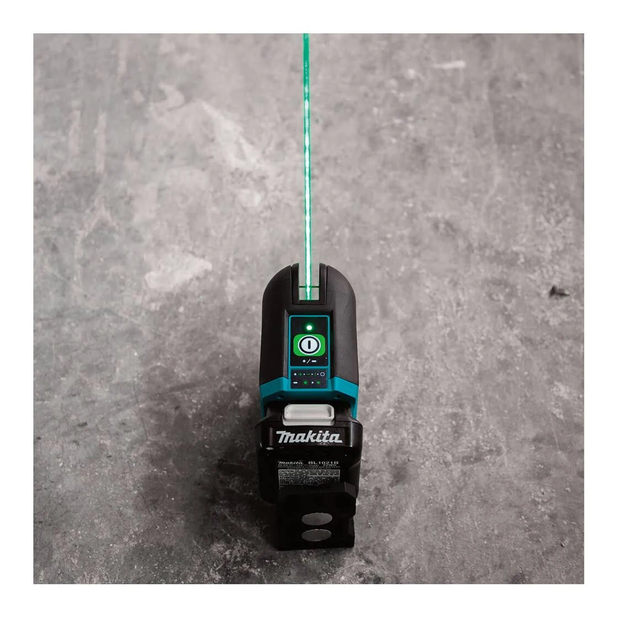Poziomica laserowa Makita, czarna i morska, z zieloną wiązką lasera. Narzędzie znajduje się na szarej powierzchni.