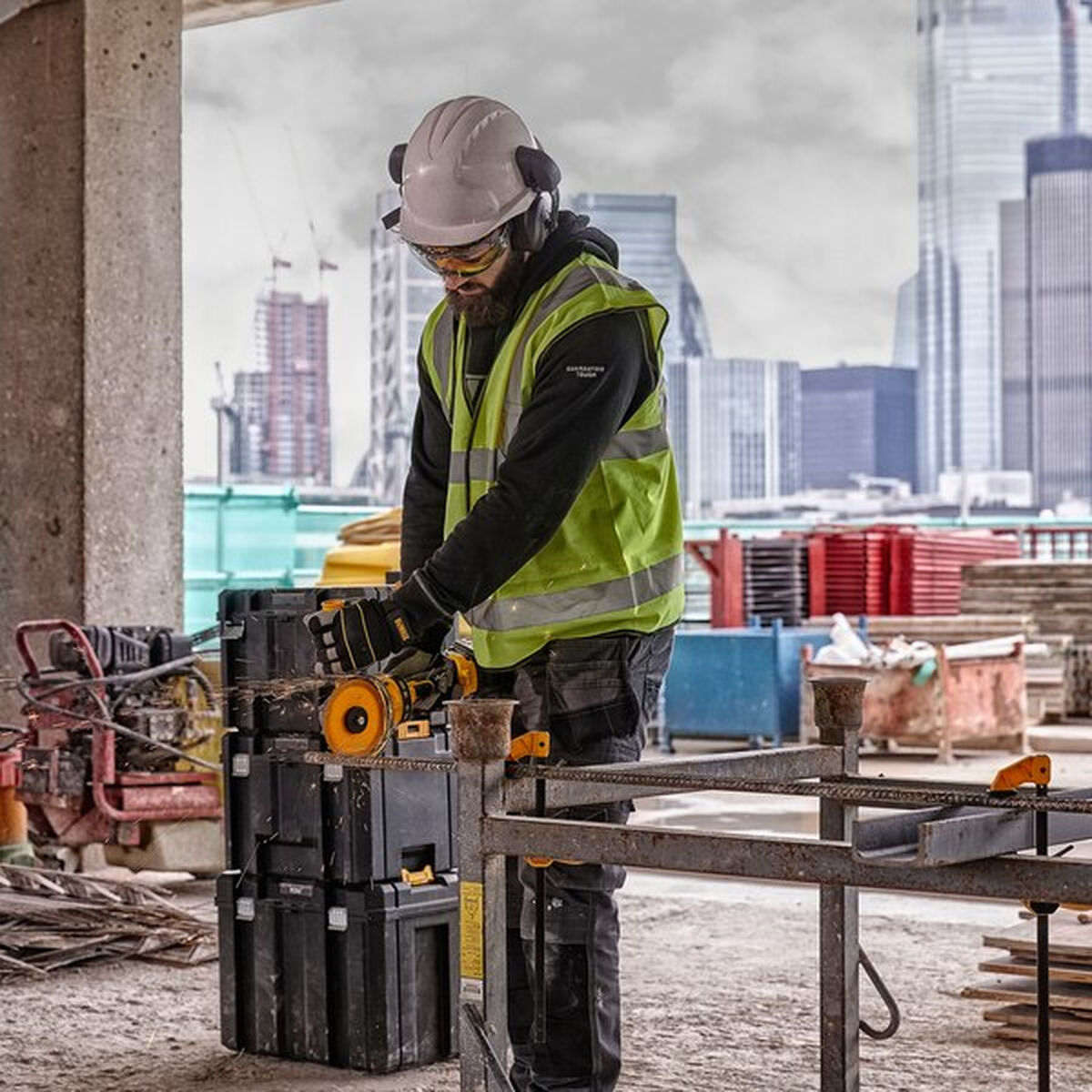Trabajador construcción usando amoladora angular. Con equipo de seguridad, esmerilando metal, ciudad de fondo.
