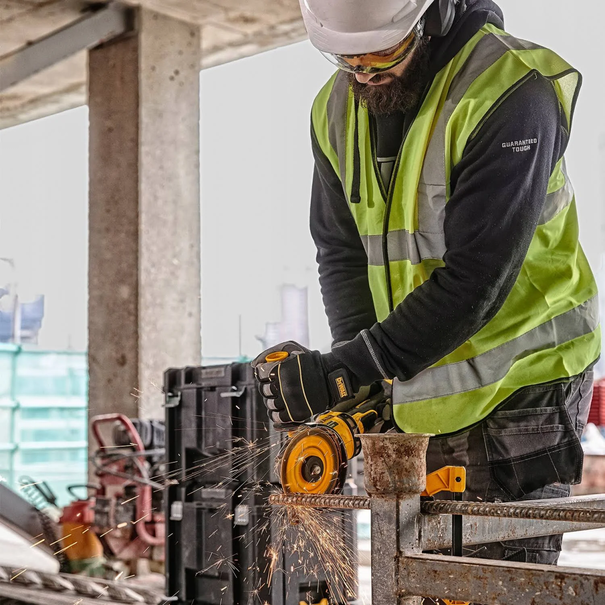 Un trabajador utiliza una amoladora angular para cortar barras de refuerzo metálicas. Lleva equipo de seguridad.