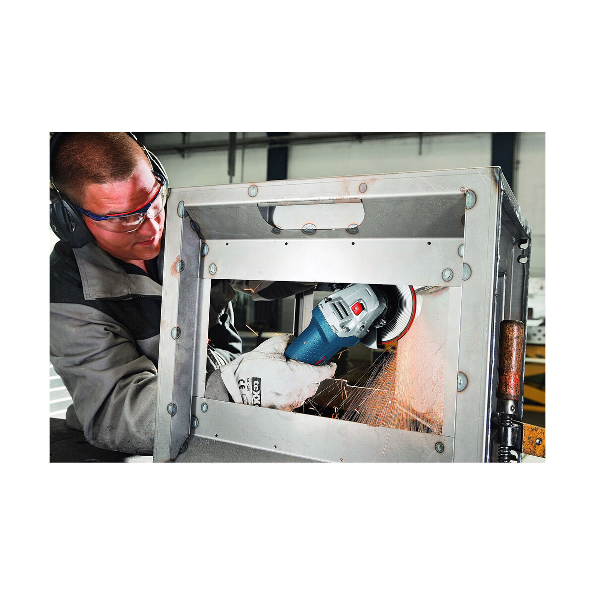 Mężczyzna używa szlifierki na metalowej konstrukcji. Nosi okulary ochronne, rękawice i ochronę słuchu.