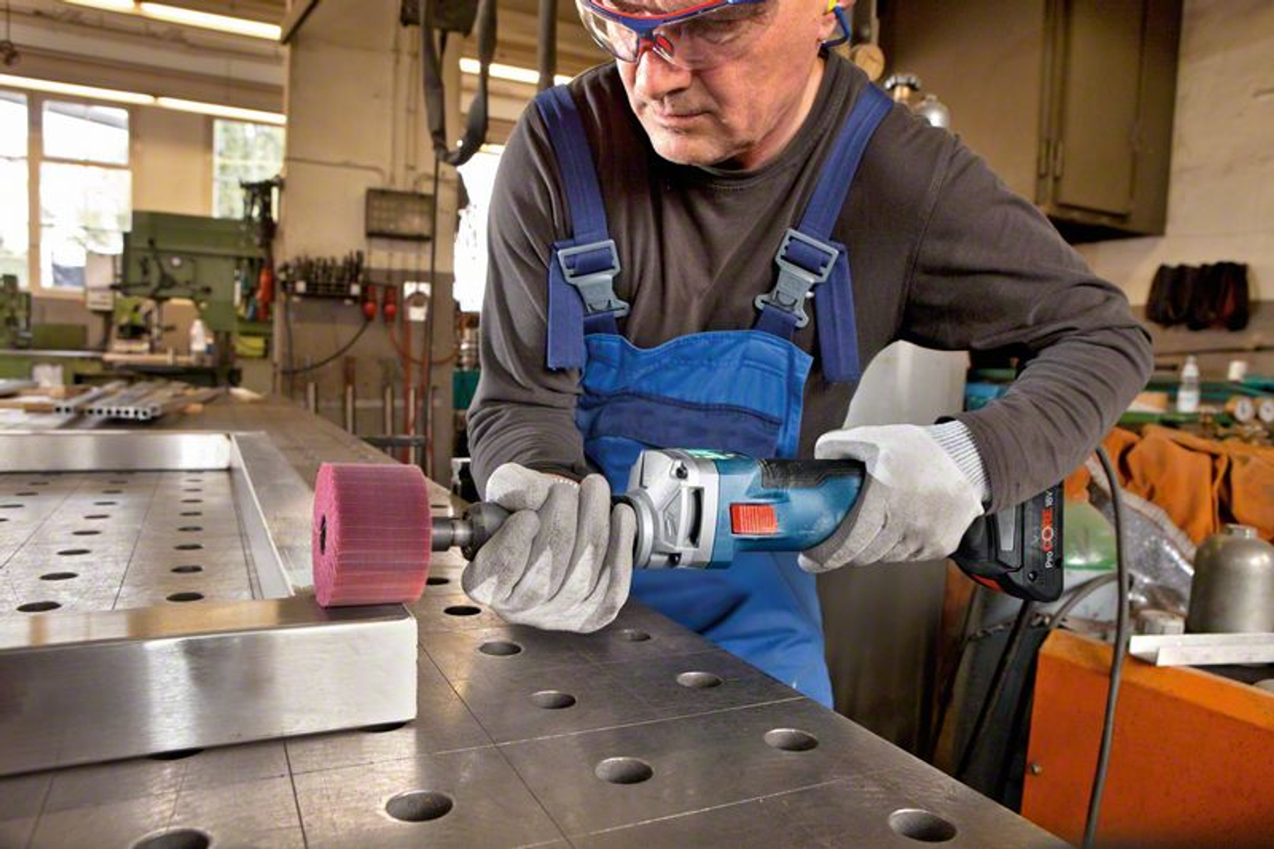 Homme utilisant une meuleuse sur du métal. Il porte des lunettes et gants de sécurité.