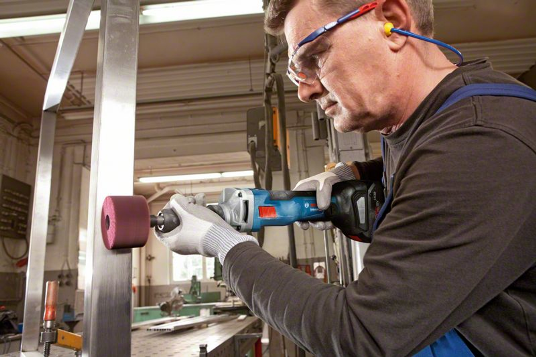 Un homme utilise une meuleuse sur une barre de métal. Il porte des lunettes et des gants de sécurité.