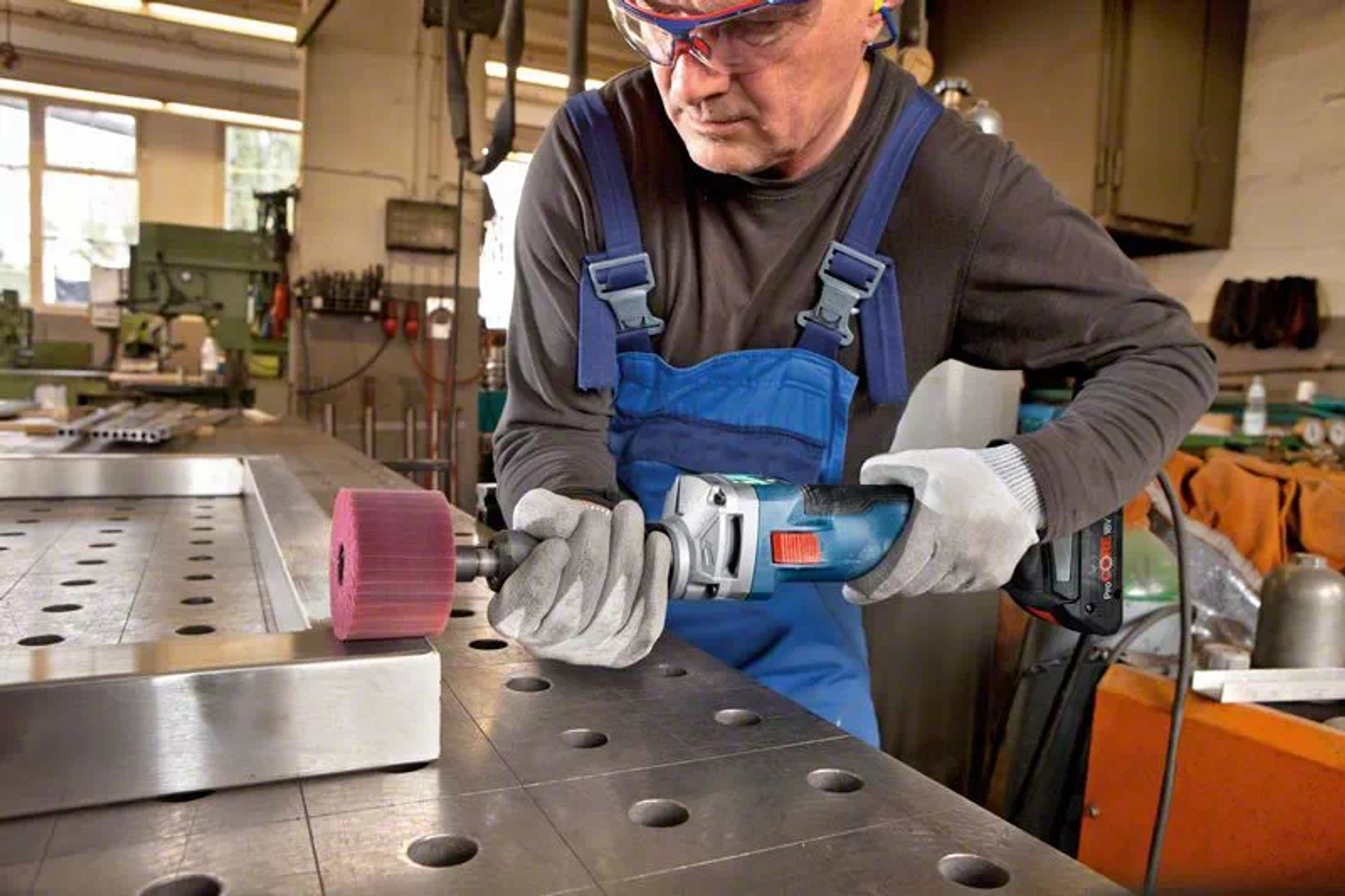 Mężczyzna używający niebiesko-srebrnego elektronarzędzia na metalowej powierzchni.