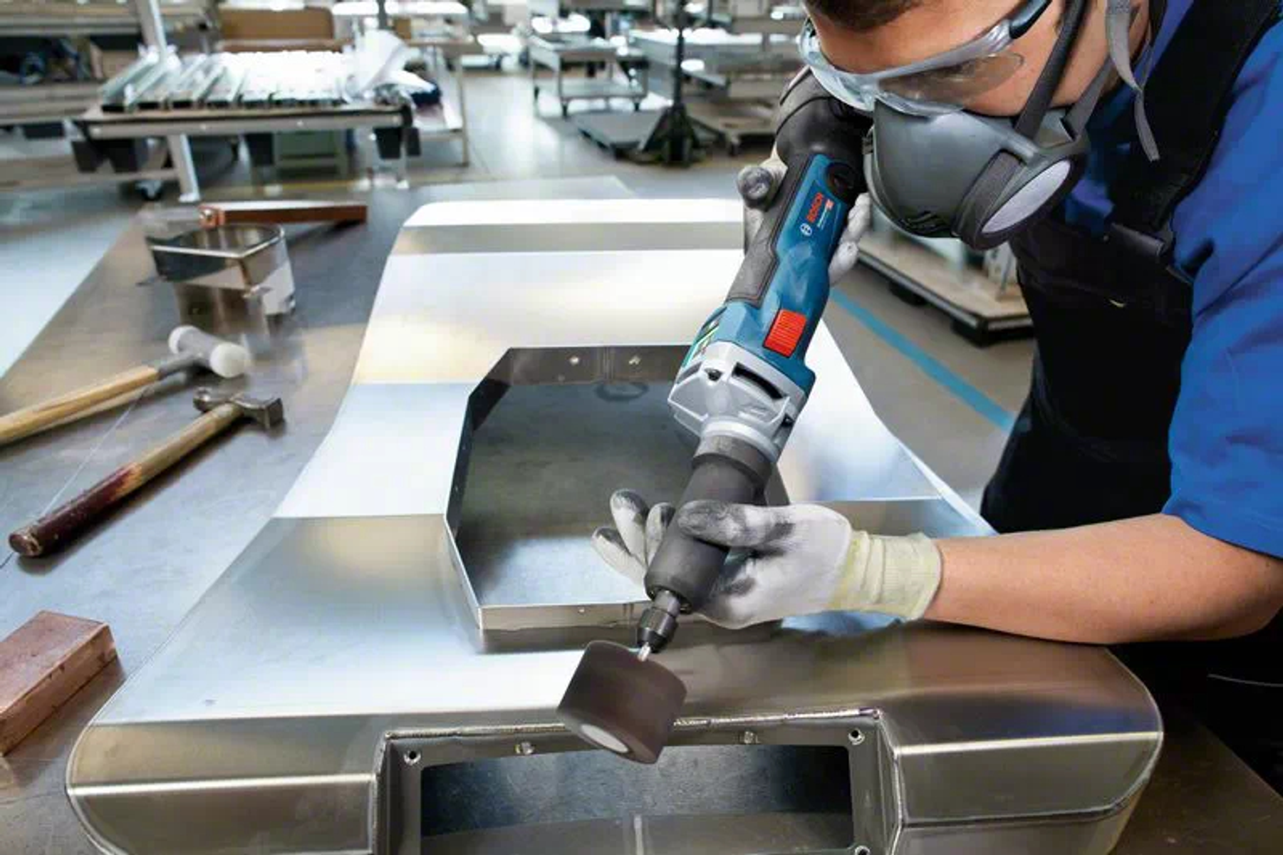 Osoba używająca szlifierki Bosch w warsztacie, ubrana w odzież ochronną.