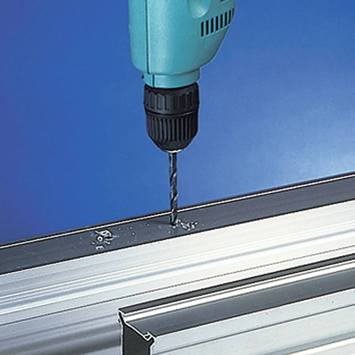 Ein blauer Bohrer bohrt in eine silberne Metallstange, vor blauem Hintergrund.