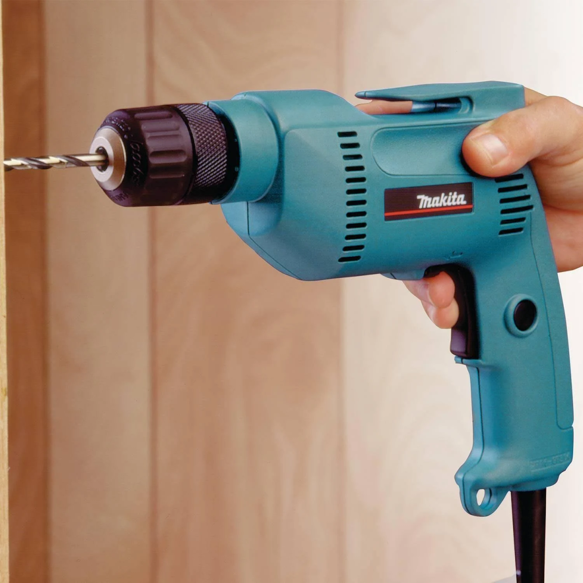 Eine türkisfarbene Makita Bohrmaschine mit einem Bohrer in einer Holzoberfläche.