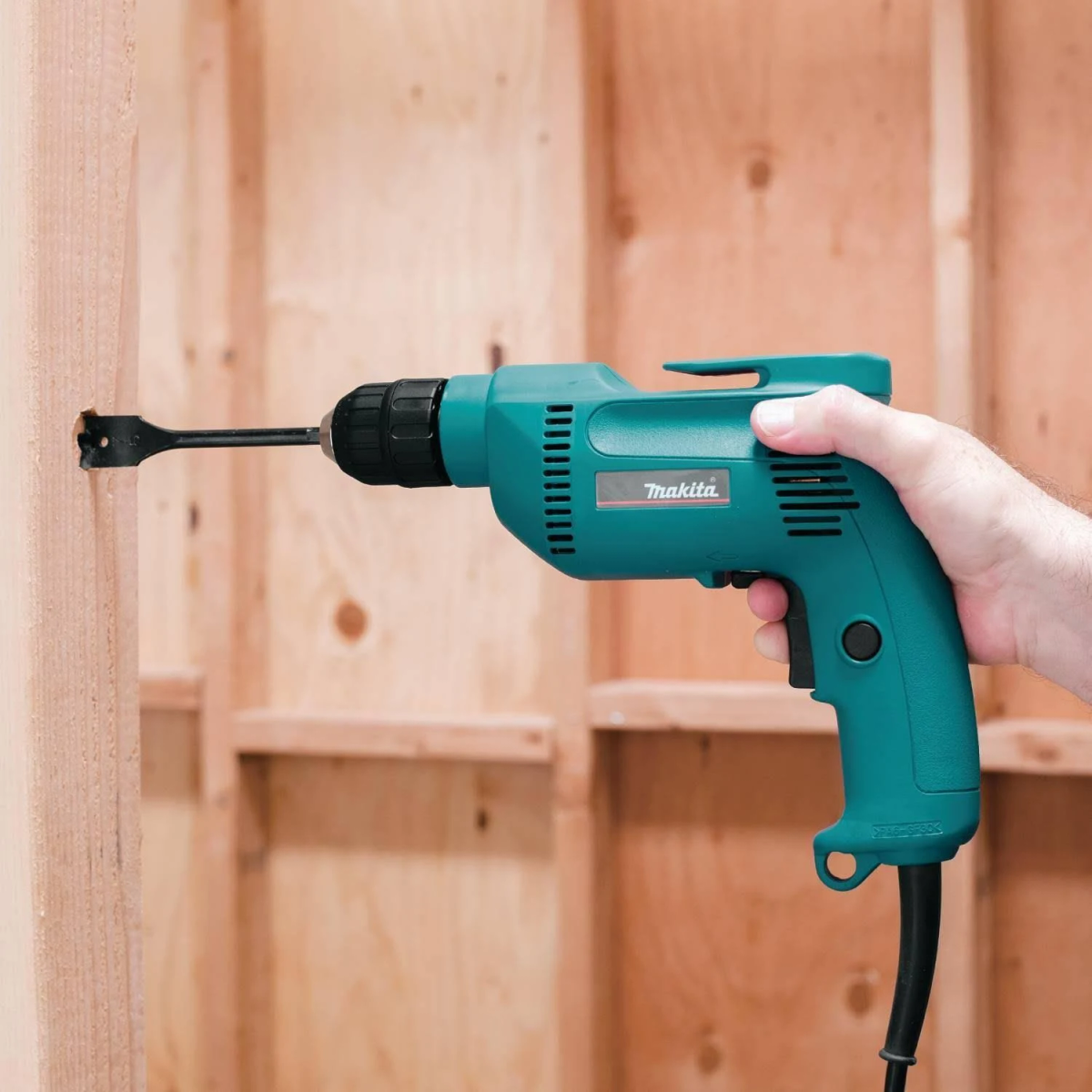 Ein Mann benutzt eine grüne Makita Bohrmaschine, um in eine Holzständerwand zu bohren.