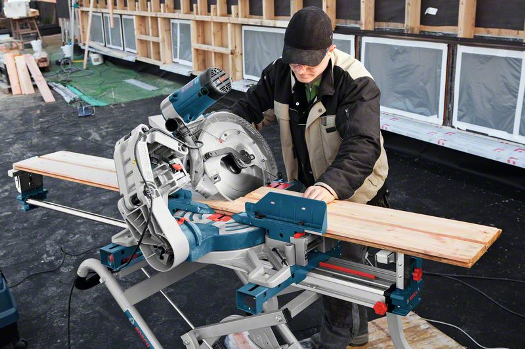 Person sägt mit einer blau-silbernen Säge eine Holzplanke auf einem Arbeitstisch.