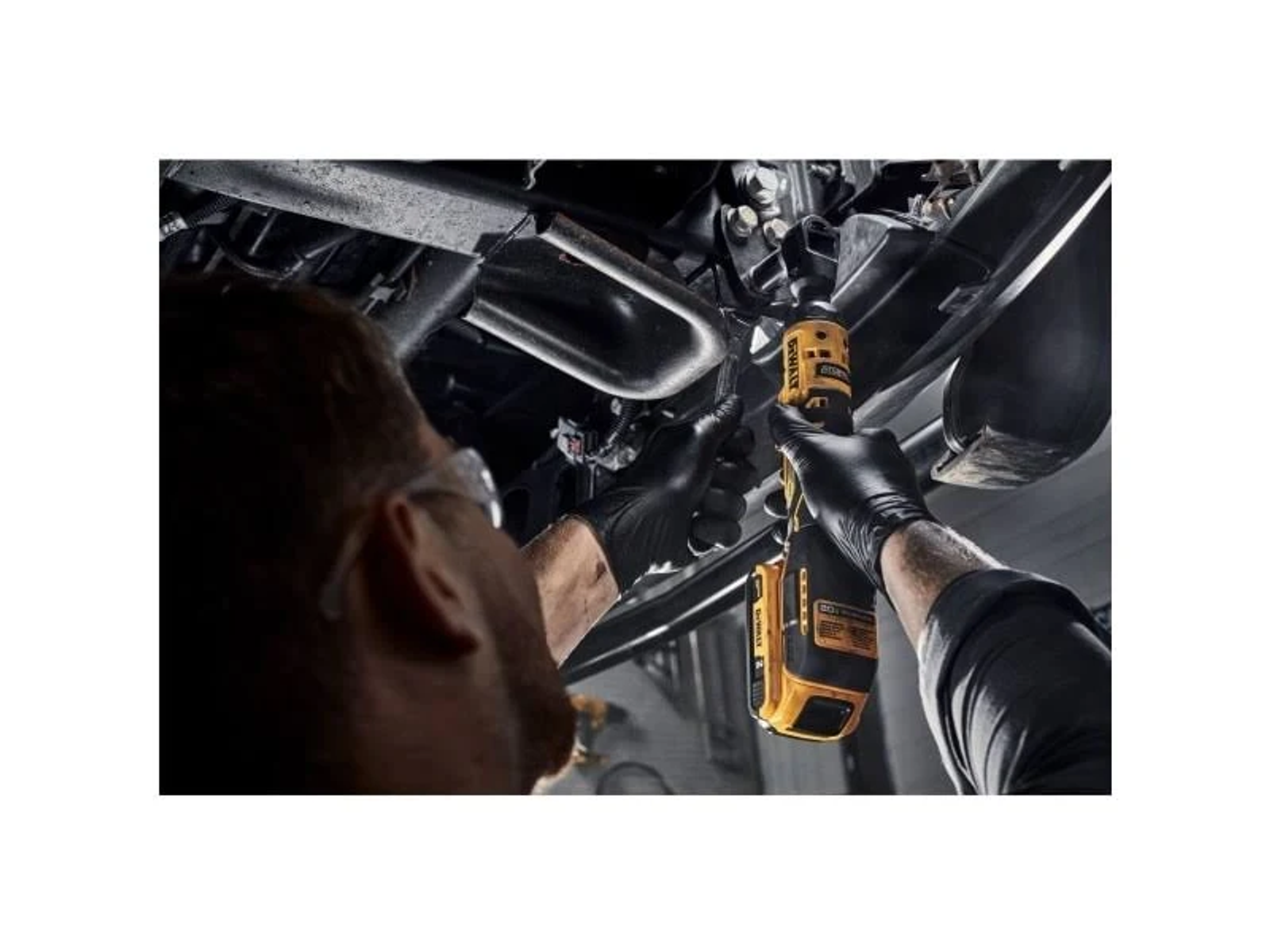 Una persona usa una llave de impacto DeWalt amarilla y negra. Debajo de un coche.