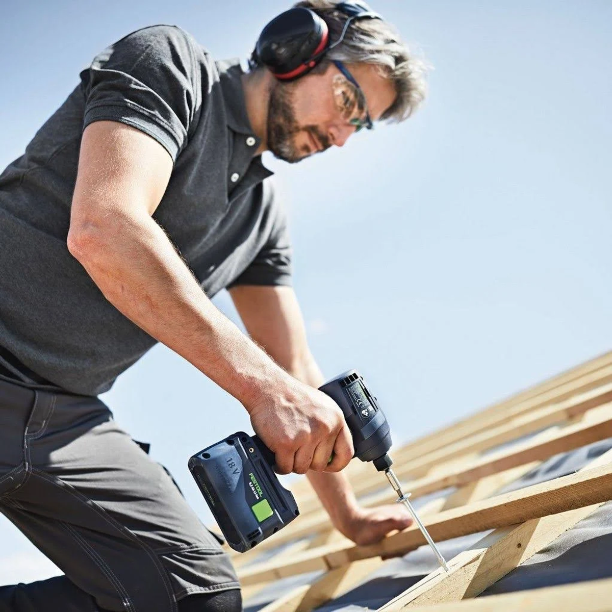 Mężczyzna używa wkrętarki udarowej Festool na dachu, nosząc ochronę słuchu.