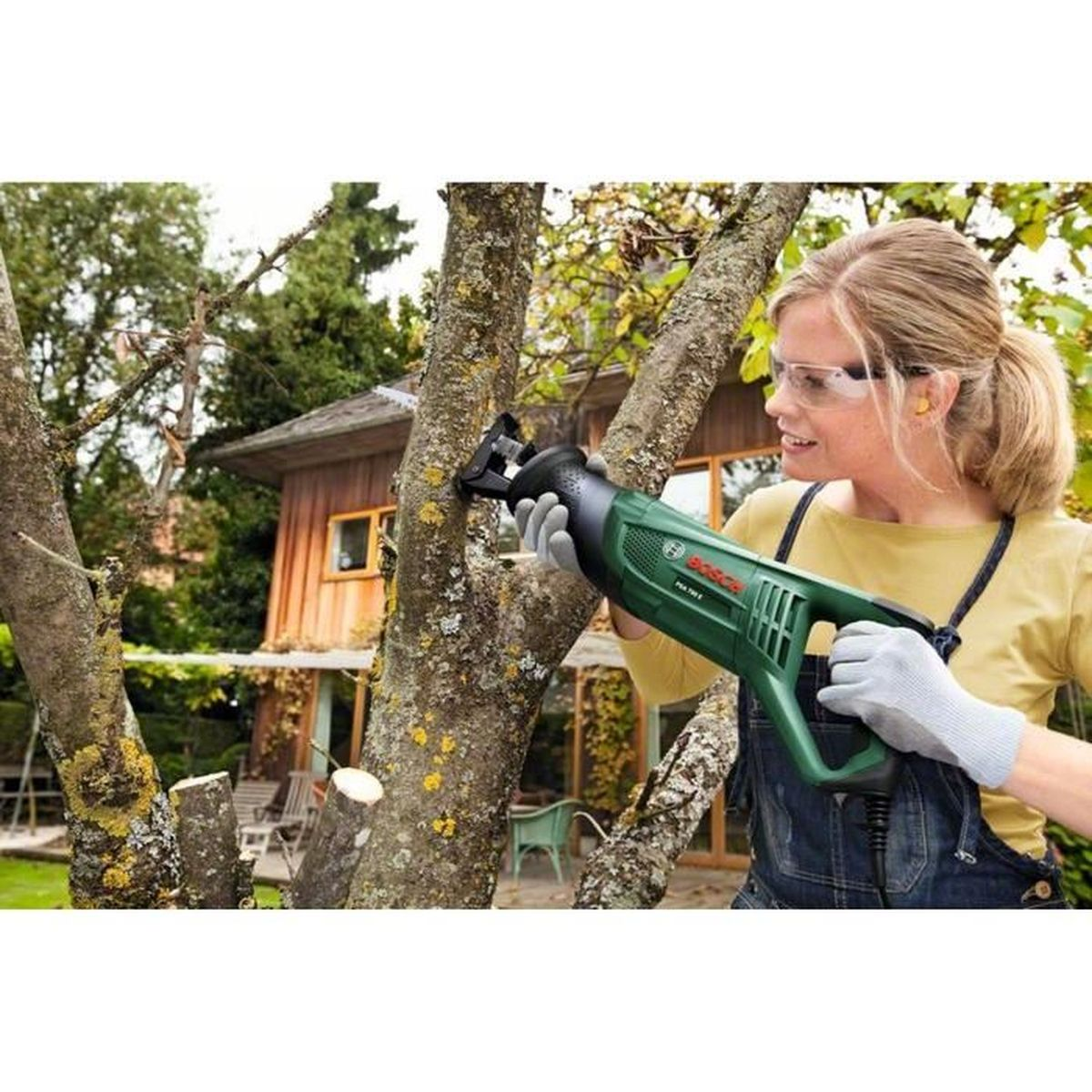 Kobieta używająca zielonej piły szablasta Bosch do cięcia gałęzi.