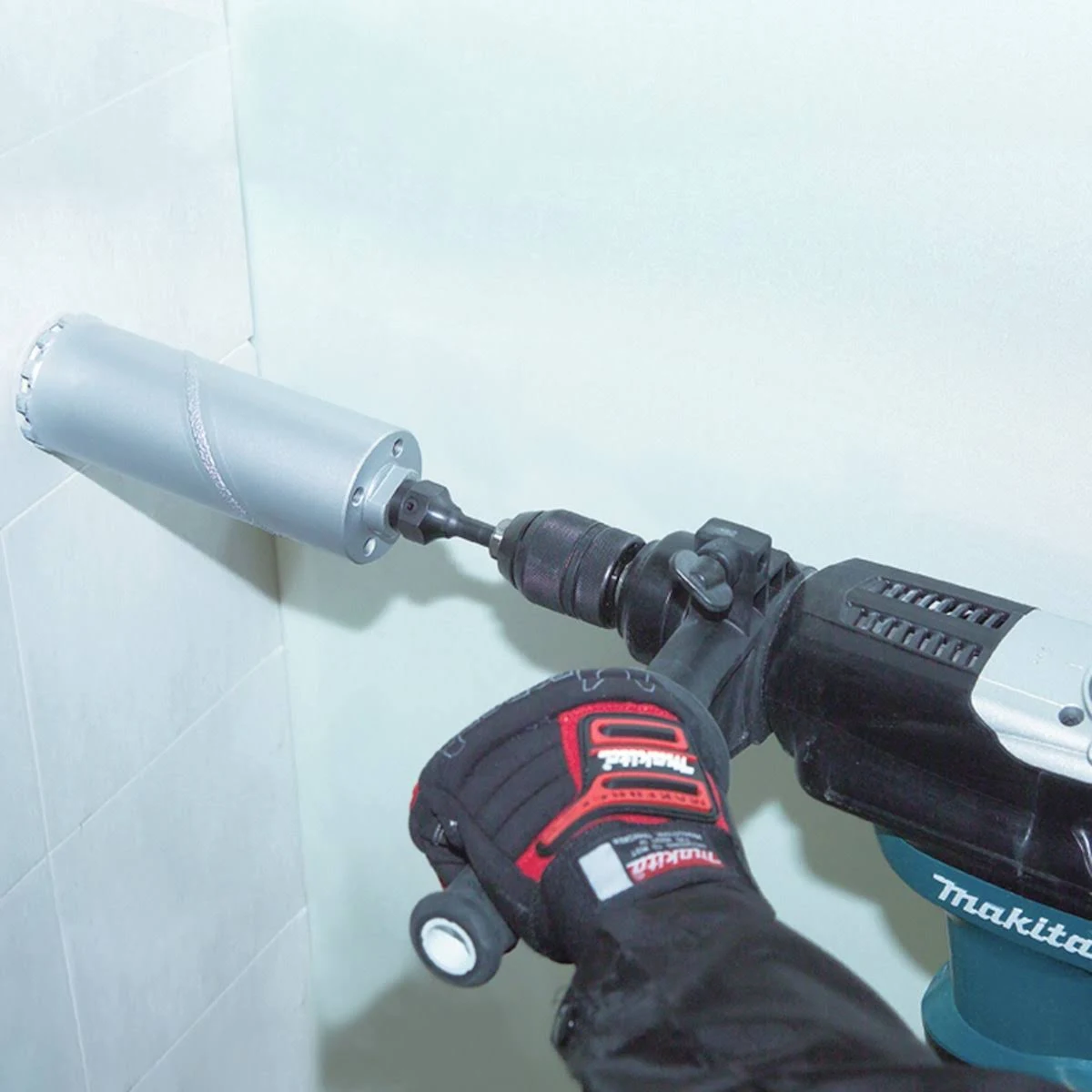 Un trabajador utiliza un taladro con una broca grande para hacer un agujero en una pared de azulejos blancos.