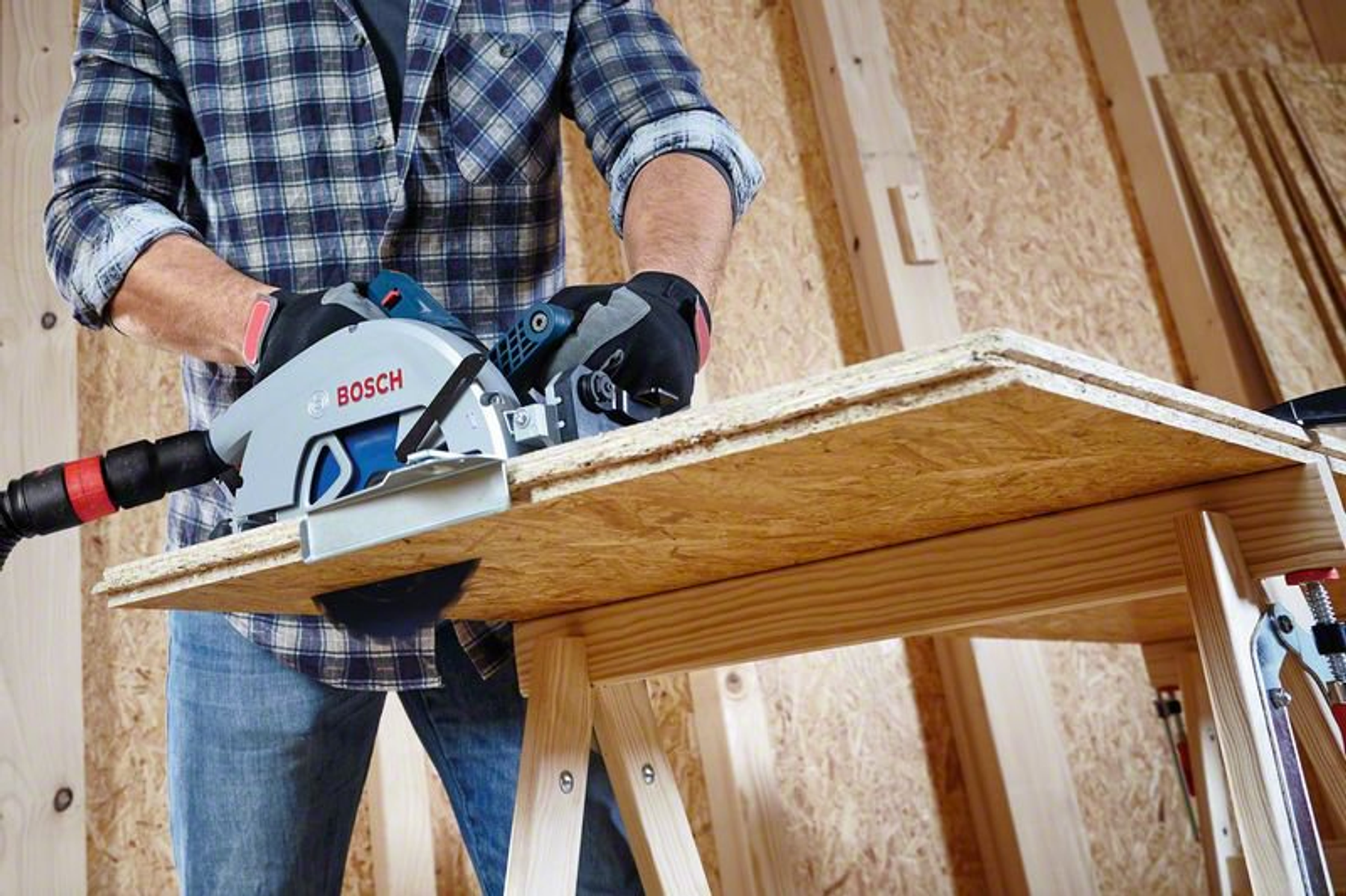 Un hombre usa una sierra circular Bosch para cortar madera en un banco de trabajo de madera en un taller.