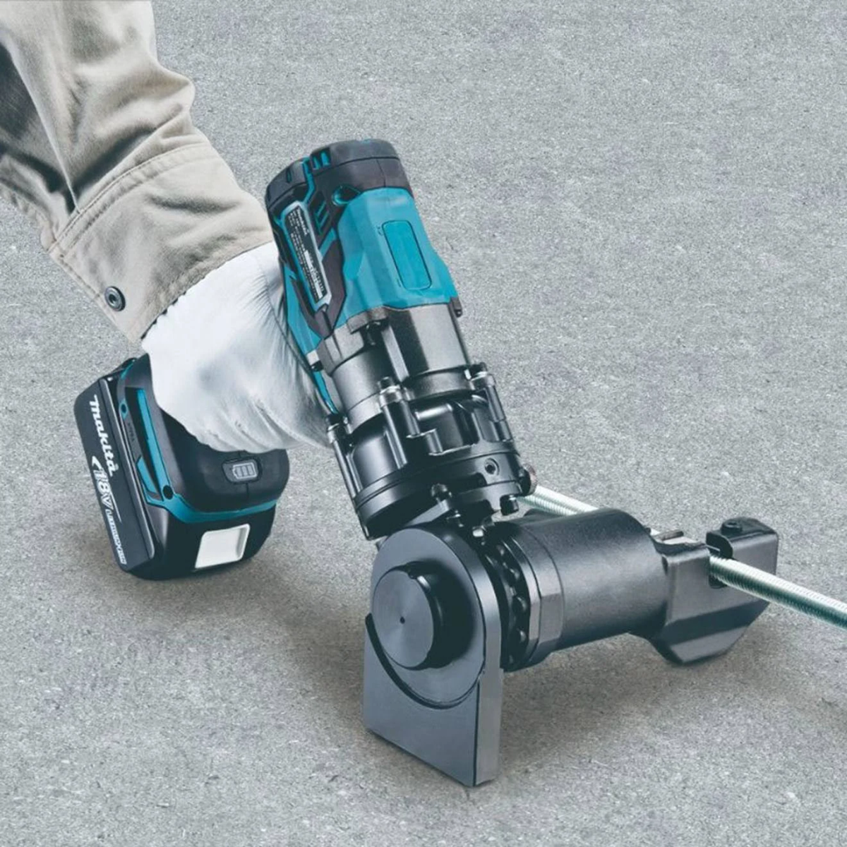 Hand hält eine teal- und schwarze Makita-Blechschere, die auf einer Betonoberfläche schneidet.