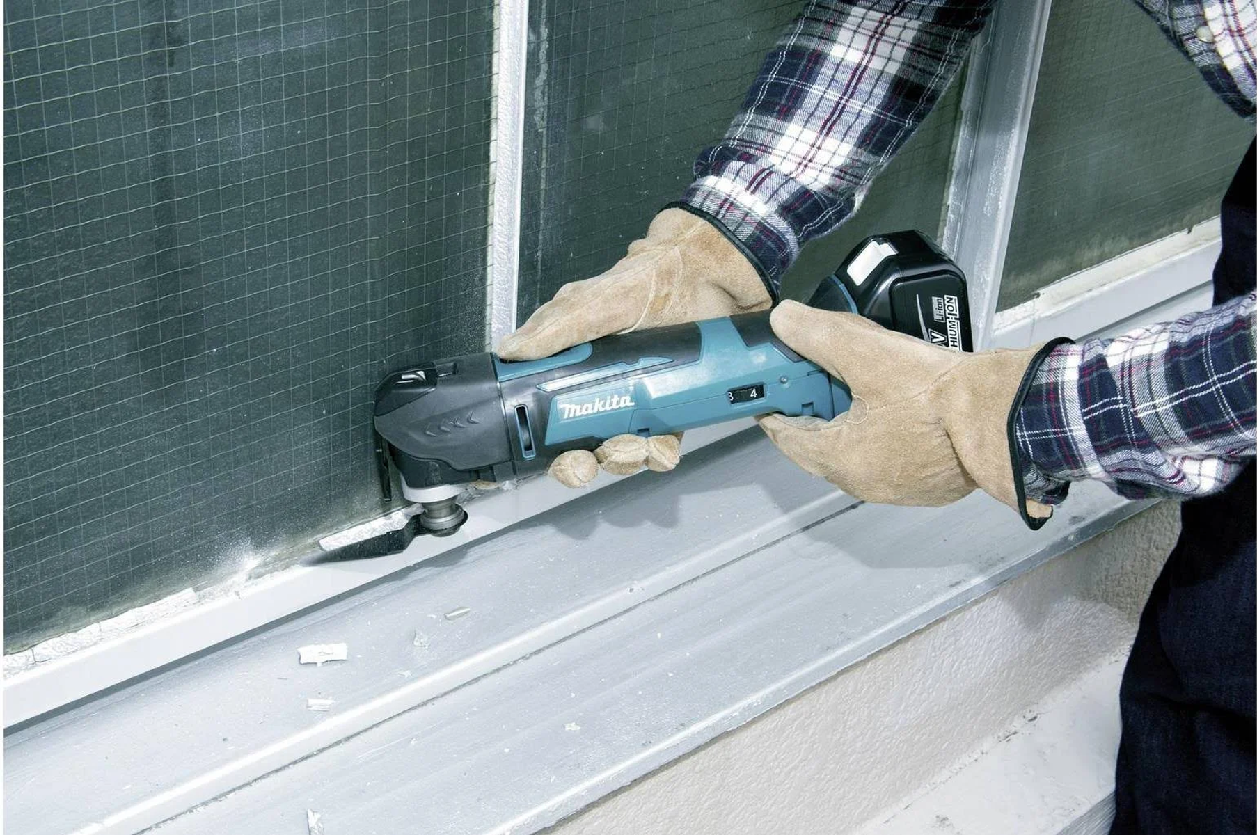 Una persona che utilizza un multiutensile Makita per tagliare un telaio della finestra.