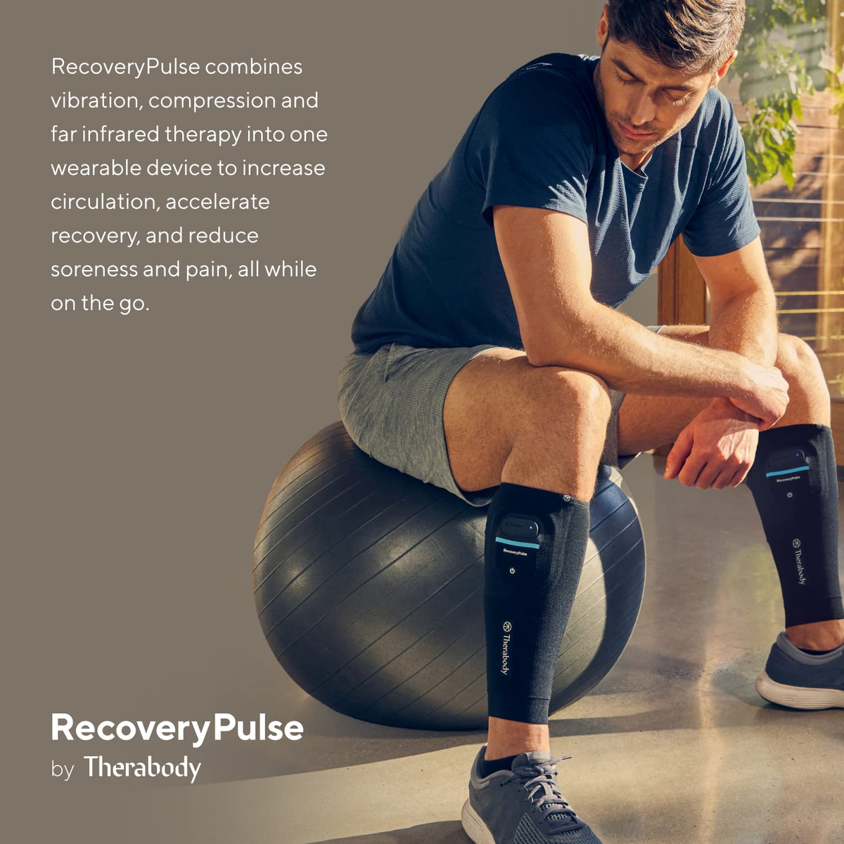 Un hombre con un dispositivo RecoveryPulse en las piernas, sentado en una pelota, en interiores.