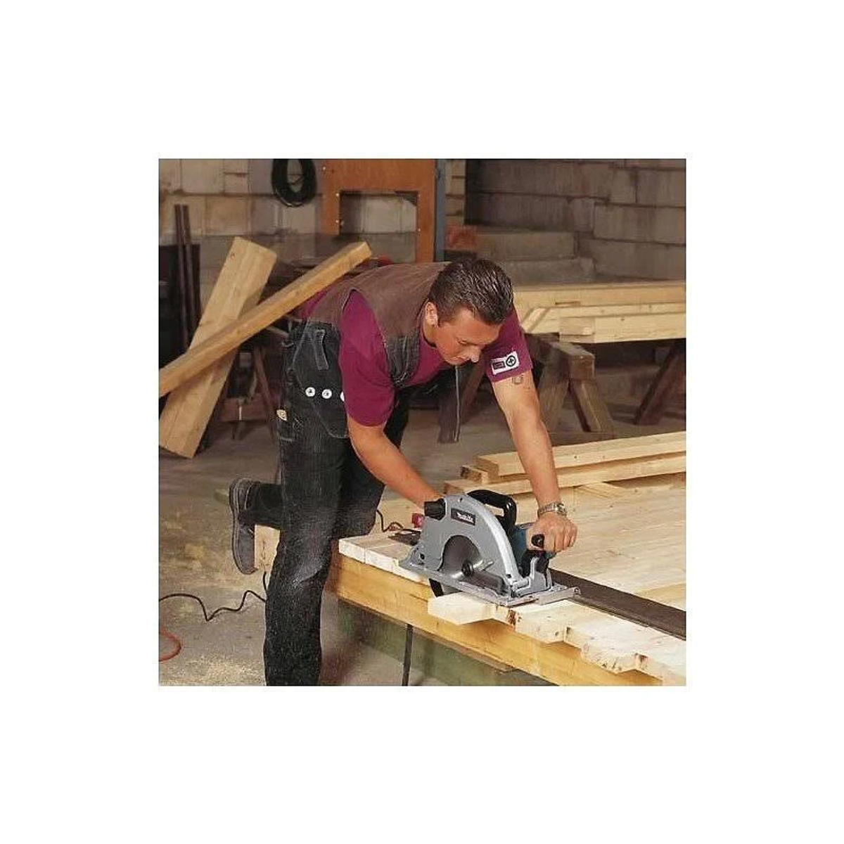 Mężczyzna używający piły tarczowej do drewna. Ma na sobie dżinsową koszulę. Piła jest Makita.