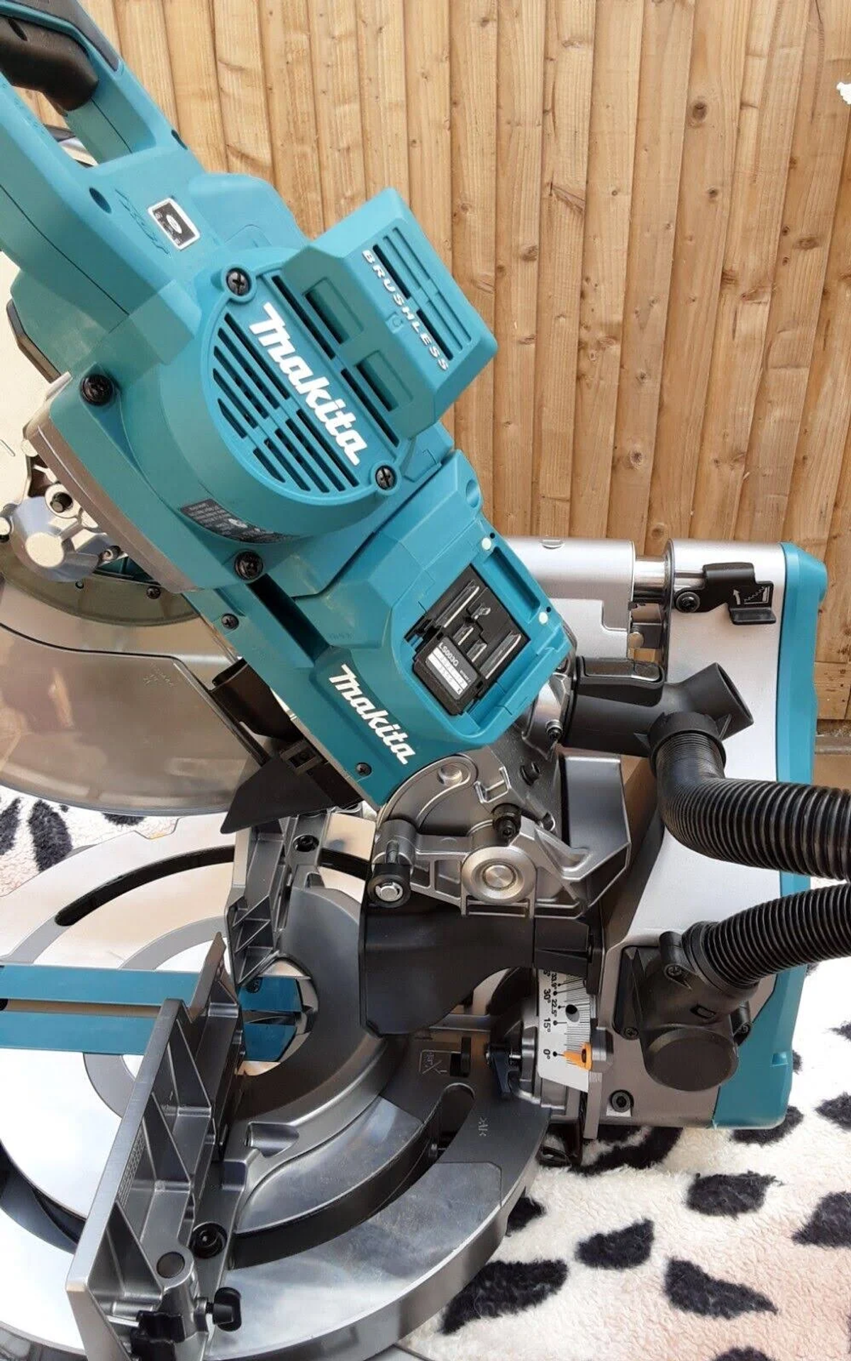 Nahaufnahme einer teal-farbenen und schwarzen Makita Gehrungsäge. Sie ist gegen Holzpaneele abgewinkelt.