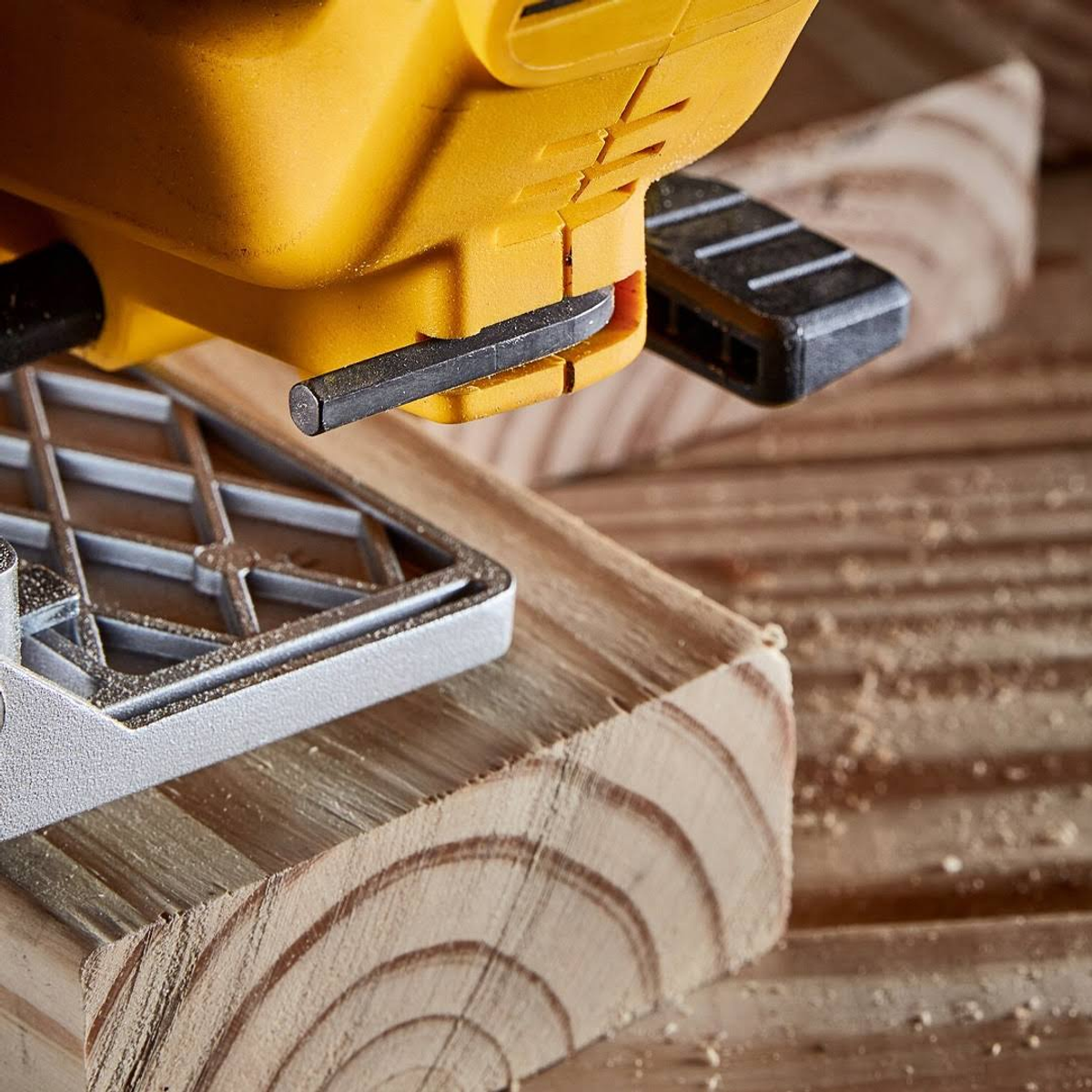 Una sierra amarilla cortando madera. La sierra está encima de tablas de madera.