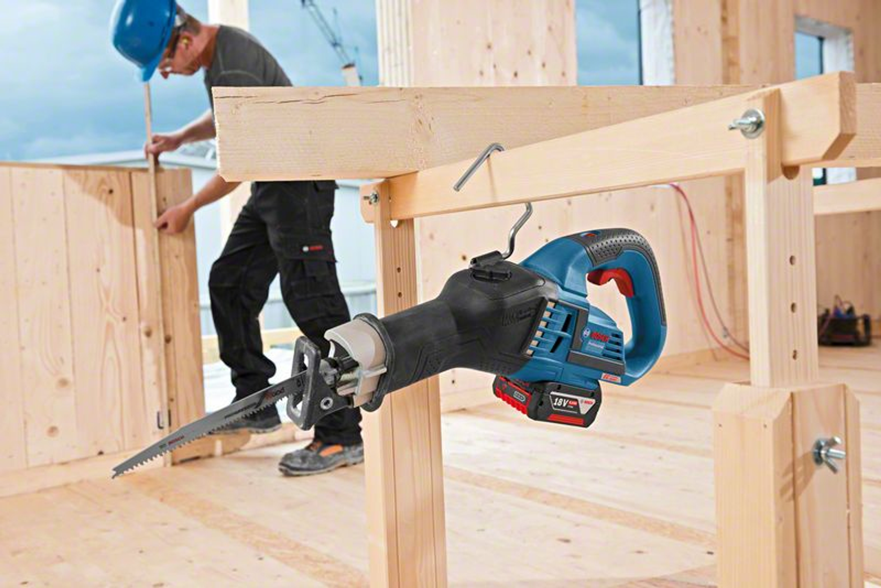 Ein Bauarbeiter, der eine Säbelsäge an einem Holzbalken verwendet. Die Säge hängt, und die Szene ist drinnen.