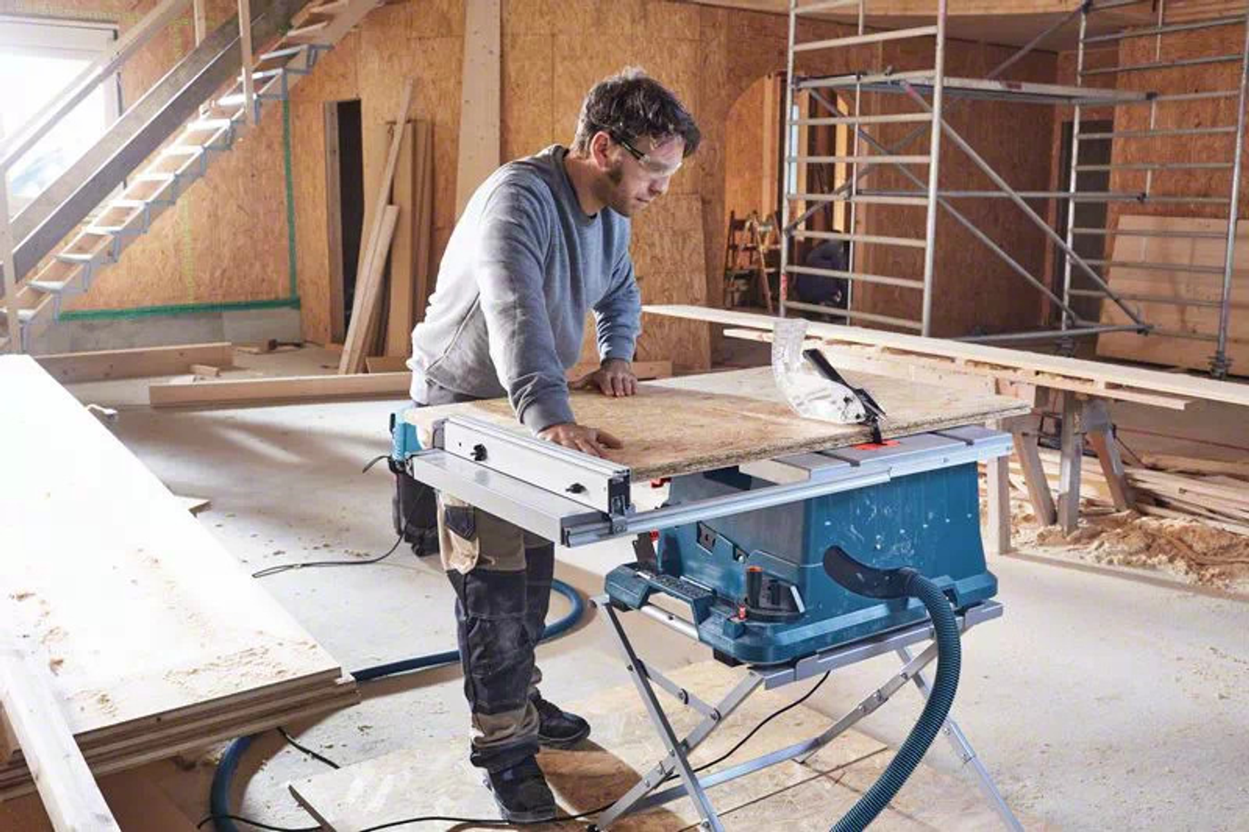 Un uomo che usa una sega da banco per tagliare il legno in un'officina. La sega è blu e argento.