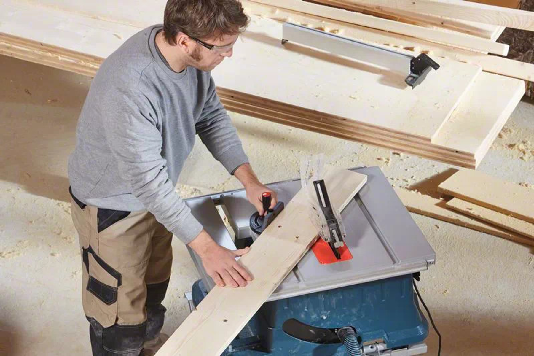 Un uomo usa una sega su un tavolo. Sta tagliando un pezzo di legno. Segatura visibile.