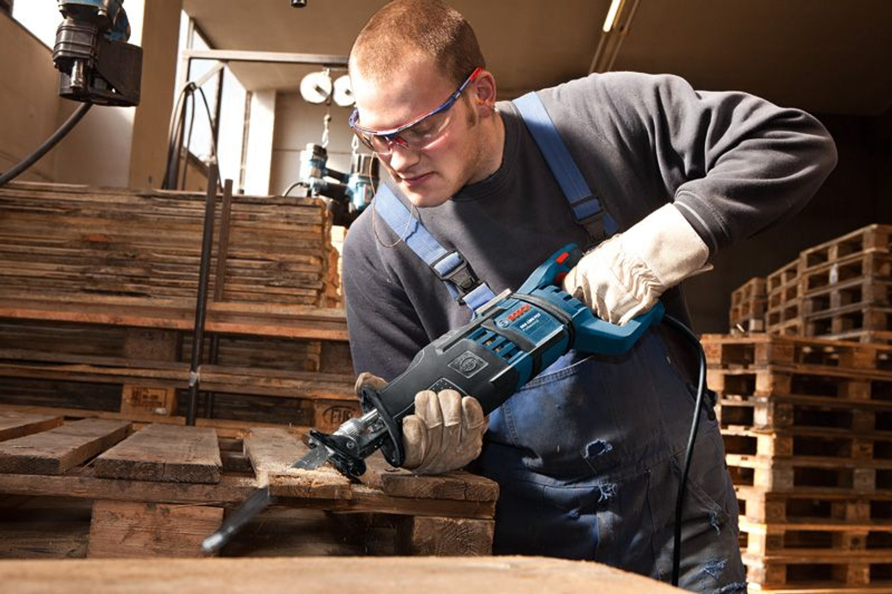 Ein Mann mit Brille benutzt eine blau-schwarze Säge, um Holz zu schneiden. Er trägt Handschuhe und Gehörschutz.
