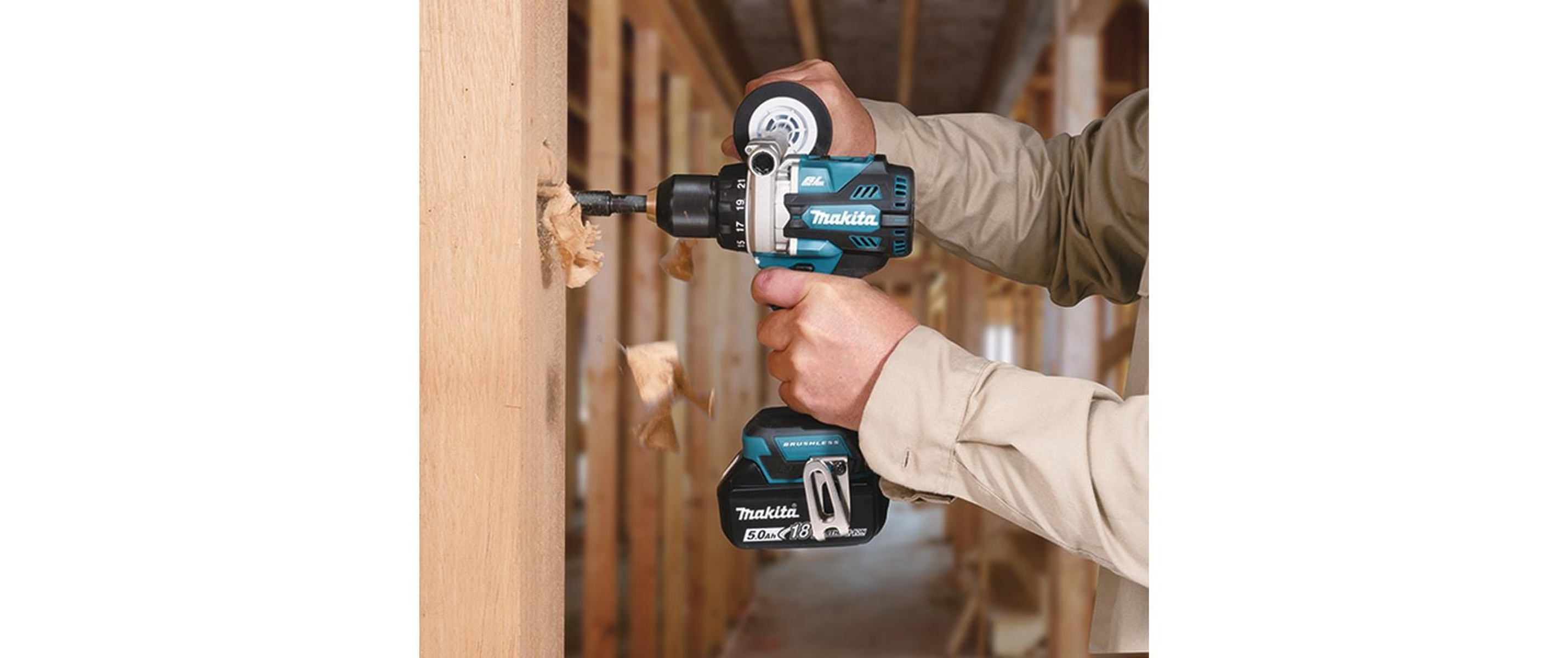 Mężczyzna wierci w drewnianej belce turkusowo-czarną wiertarką.