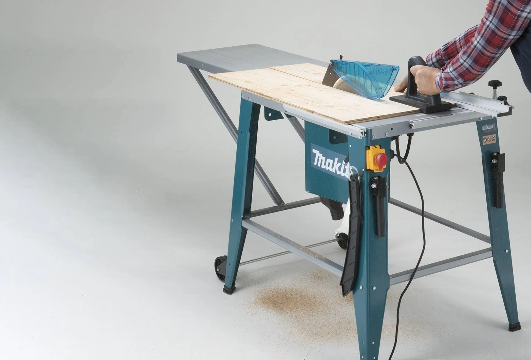 Eine Person, die eine teal Makita Tischkreissäge benutzt und Holz auf einer hellgrauen Oberfläche schneidet.
