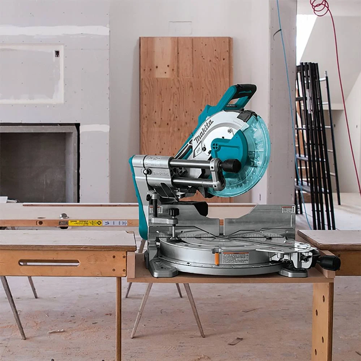 Eine teal-silberne Gehrungssäge auf einem Holztisch. Hintergrund zeigt unfertigen Bau.