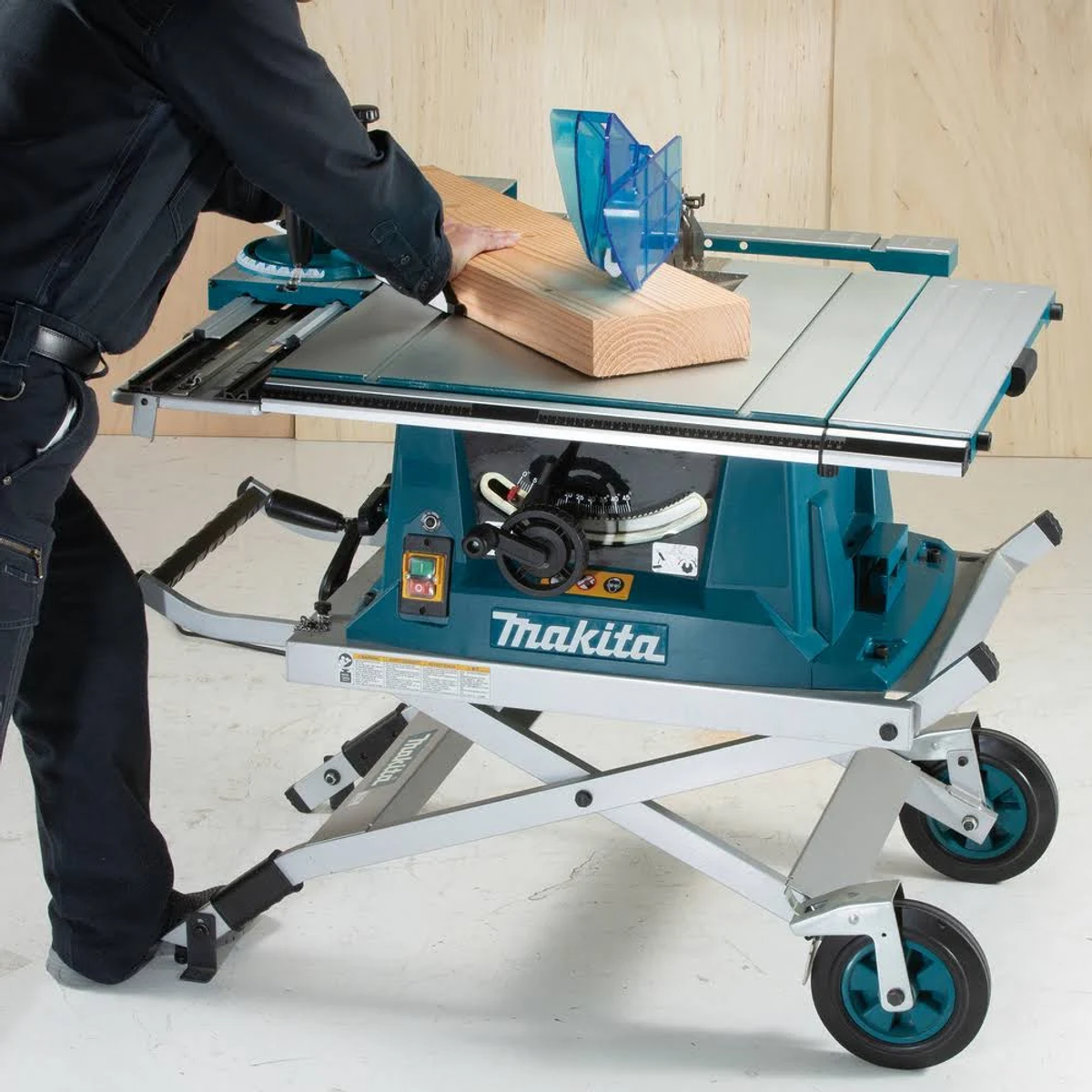 Hombre usando sierra de mesa turquesa, cortando madera. Marca Makita, fondo blanco.