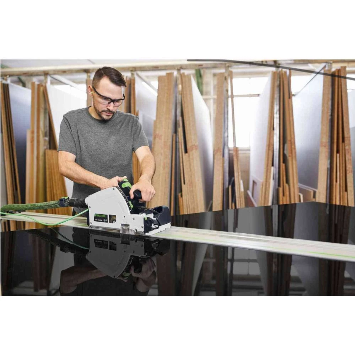 Un hombre usa una sierra Festool para cortar material negro sobre una mesa en un taller.