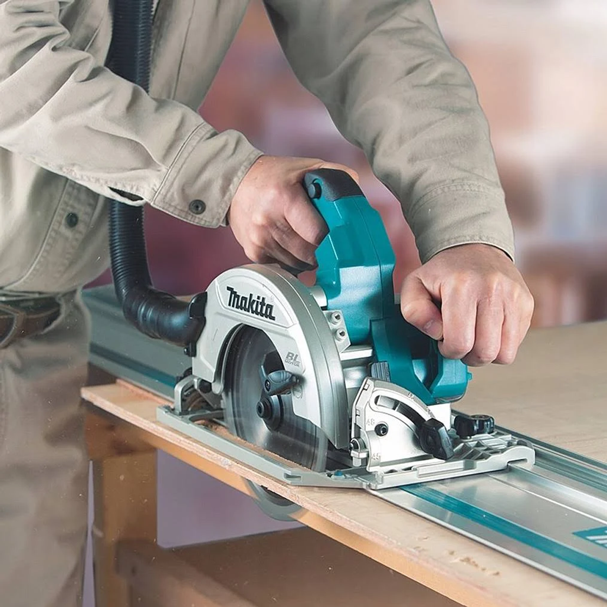 Una persona usa una sierra circular Makita en una tabla de madera. El fondo es una superficie de madera.