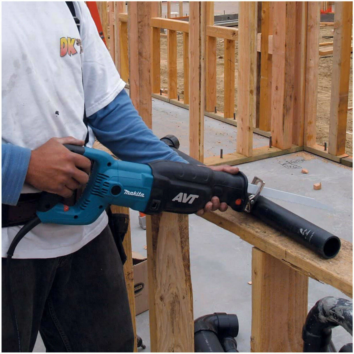 Un hombre usando una sierra recíproca turquesa y negra para cortar una tabla en un sitio de construcción.