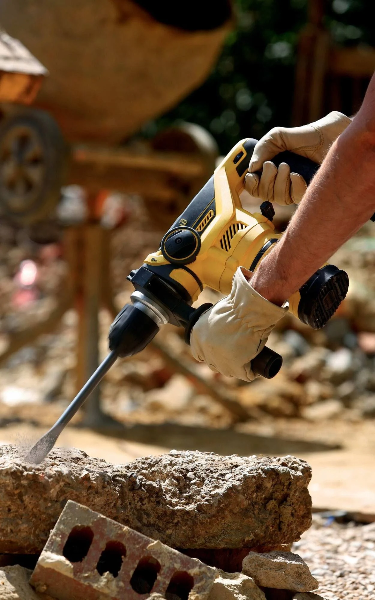 Osoba używająca żółto-czarnej wiertarki do rozbijania cegły. Otoczenie budowy.