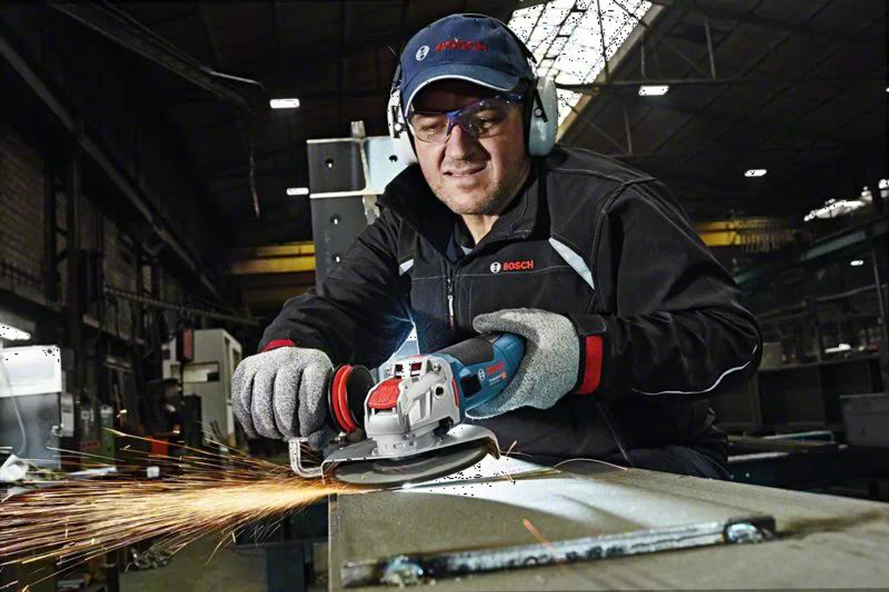 Mężczyzna szlifuje metal szlifierką kątową. Iskry lecą. Ma okulary i rękawice.