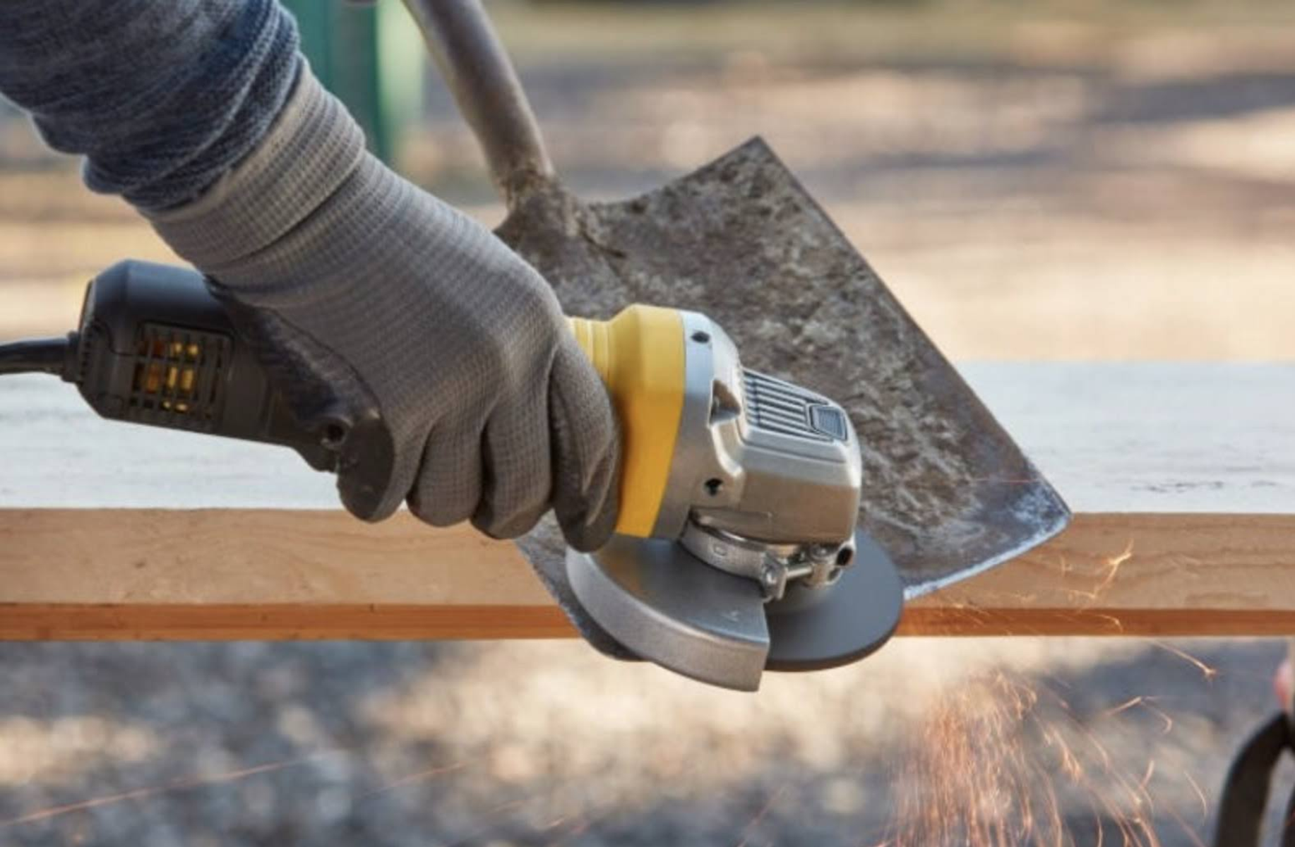 Ręka w rękawicy używa szlifierki kątowej do szlifowania łopaty, iskry lecą.