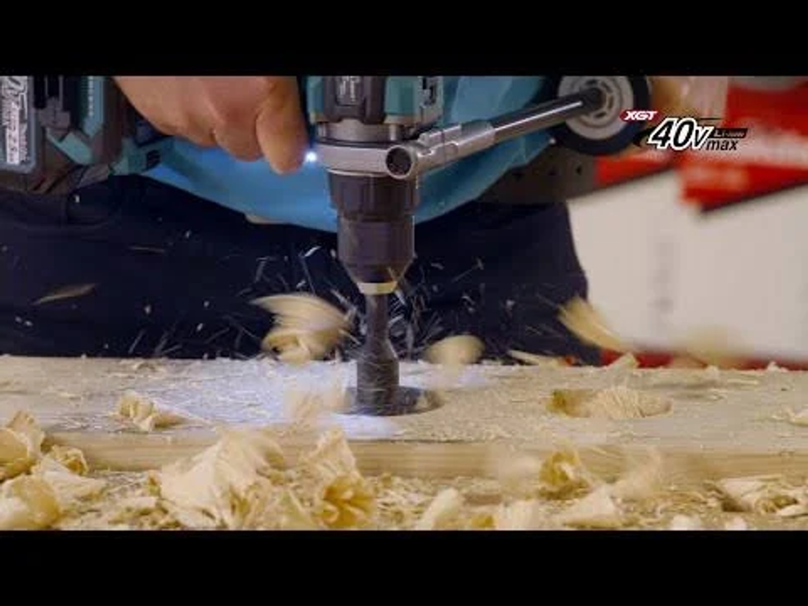 Persona perforando madera con un taladro Makita, virutas de madera visibles. XGT 40v max visible.