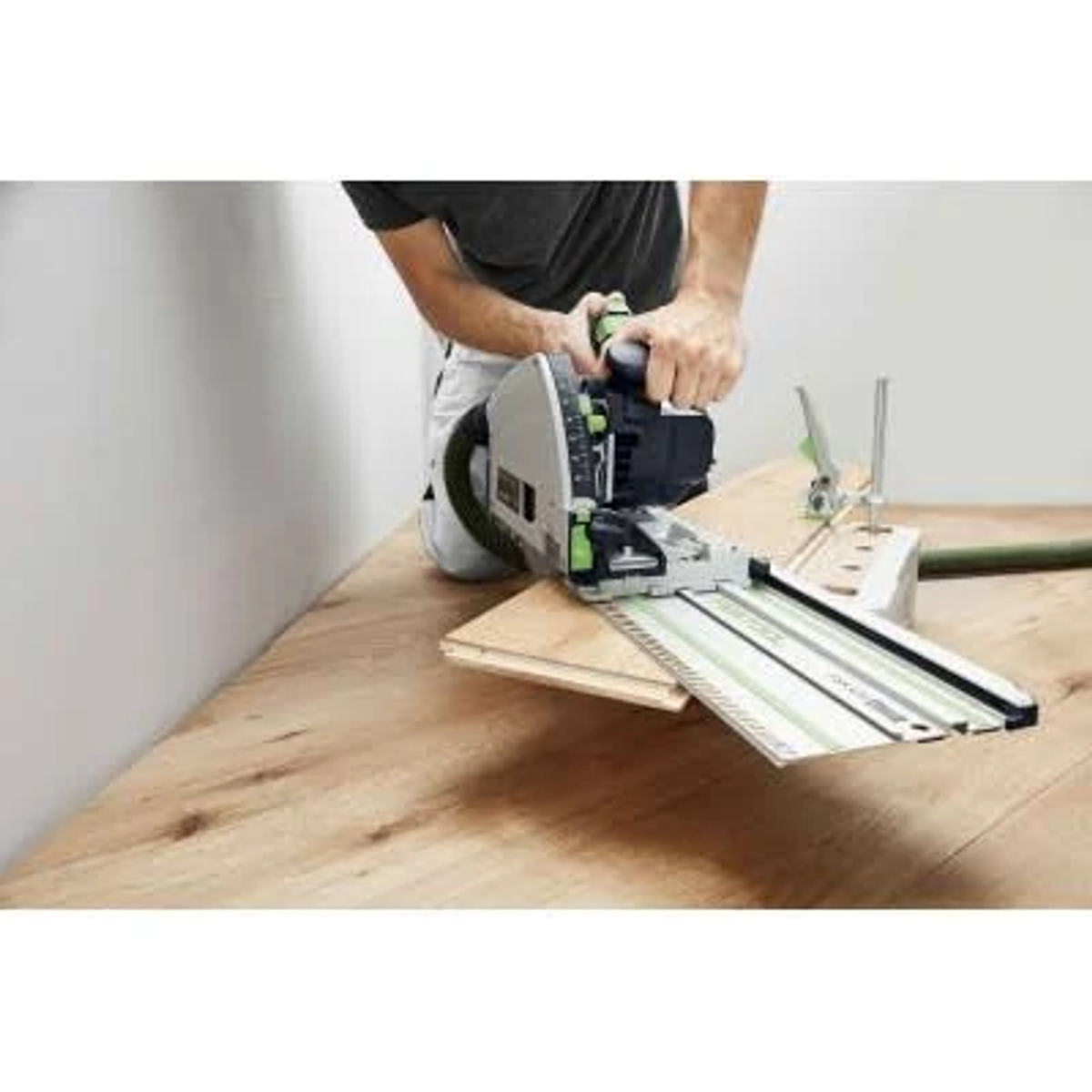 Un hombre usa una sierra Festool para cortar madera sobre una superficie de madera en un taller.