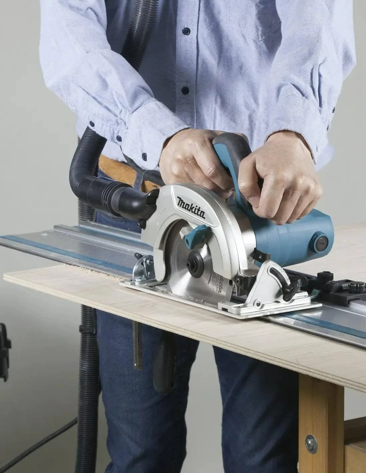 Osoba używająca piły tarczowej na drewnianej powierzchni. Piła jest turkusowa i srebrna.