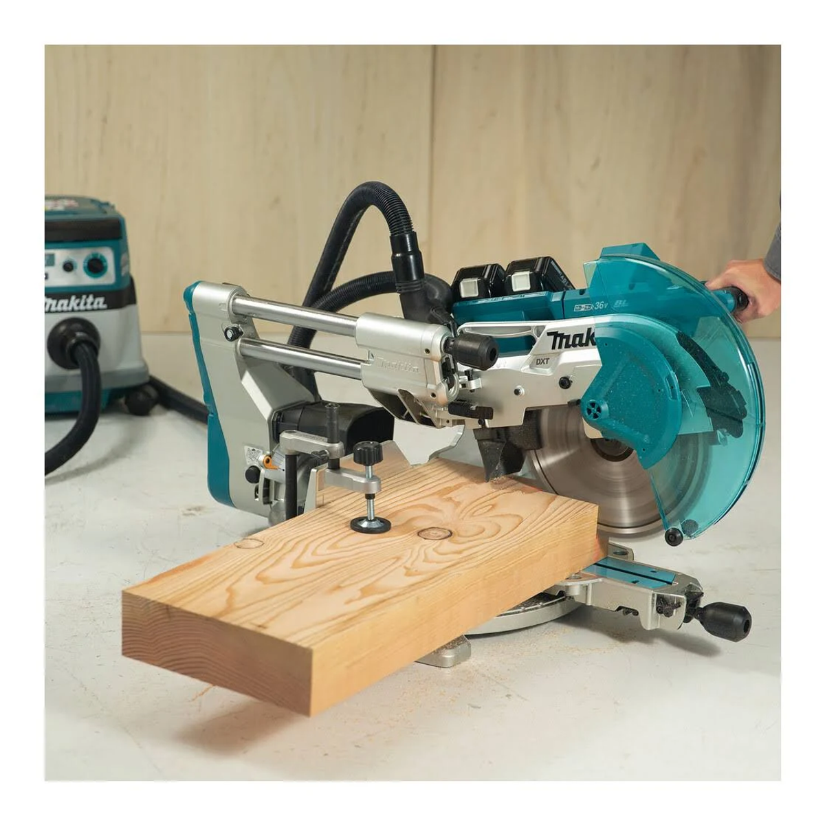 Makita-Gehrungssäge schneidet einen Holzbalken. Hellblaue und graue Säge, mit Staubsauger im Hintergrund.
