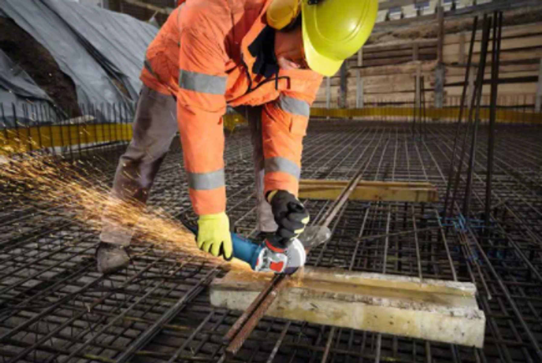 Un trabajador esmerila barras de refuerzo en una obra con una amoladora angular. Saltan chispas.