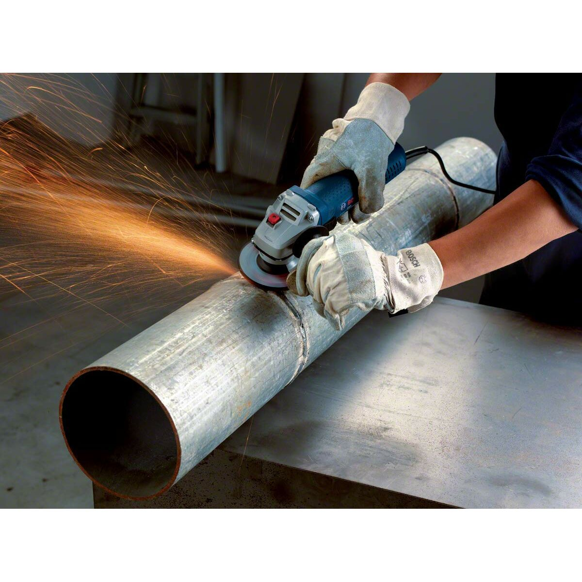 Osoba szlifuje metalową rurę szlifierką, lecą iskry.
