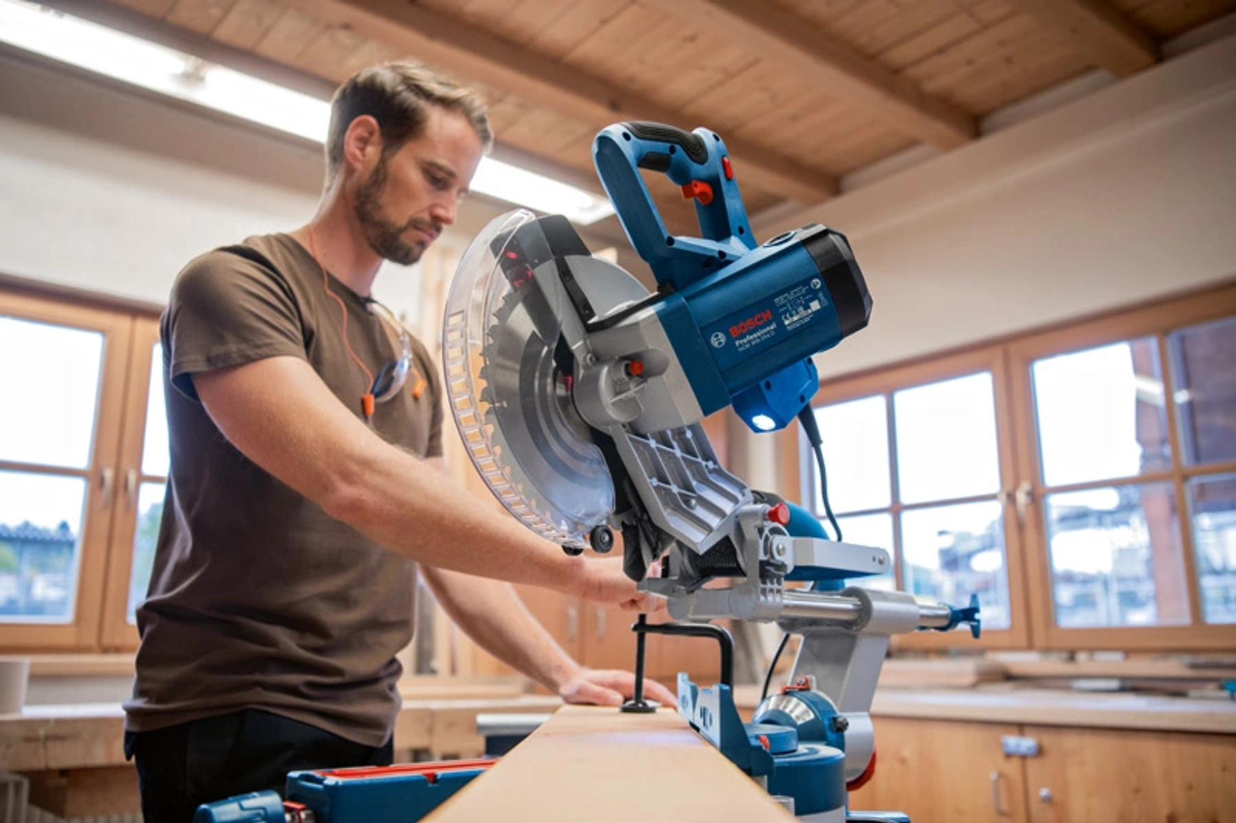Hombre usando sierra azul Bosch, trabajando en viga de madera en taller.
