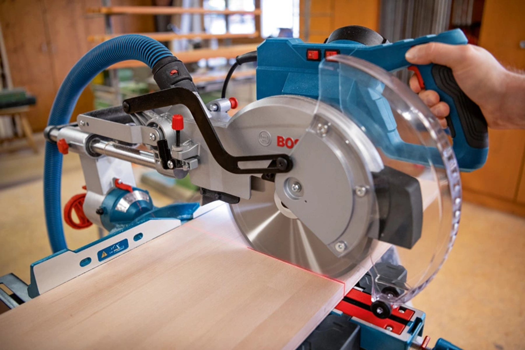 Una persona usando una sierra ingletadora Bosch para cortar un trozo de madera, entorno de taller.