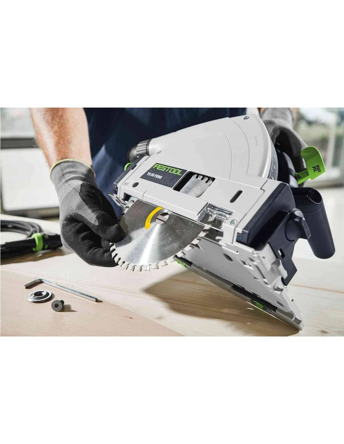 Primer plano de una sierra circular Festool cortando madera. La hoja de sierra es visible. Fondo es superficie de madera.