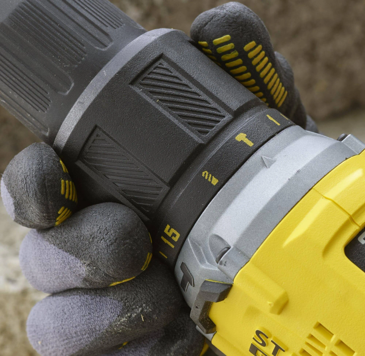 Primer plano de una mano con guantes sujetando un taladro amarillo y negro.