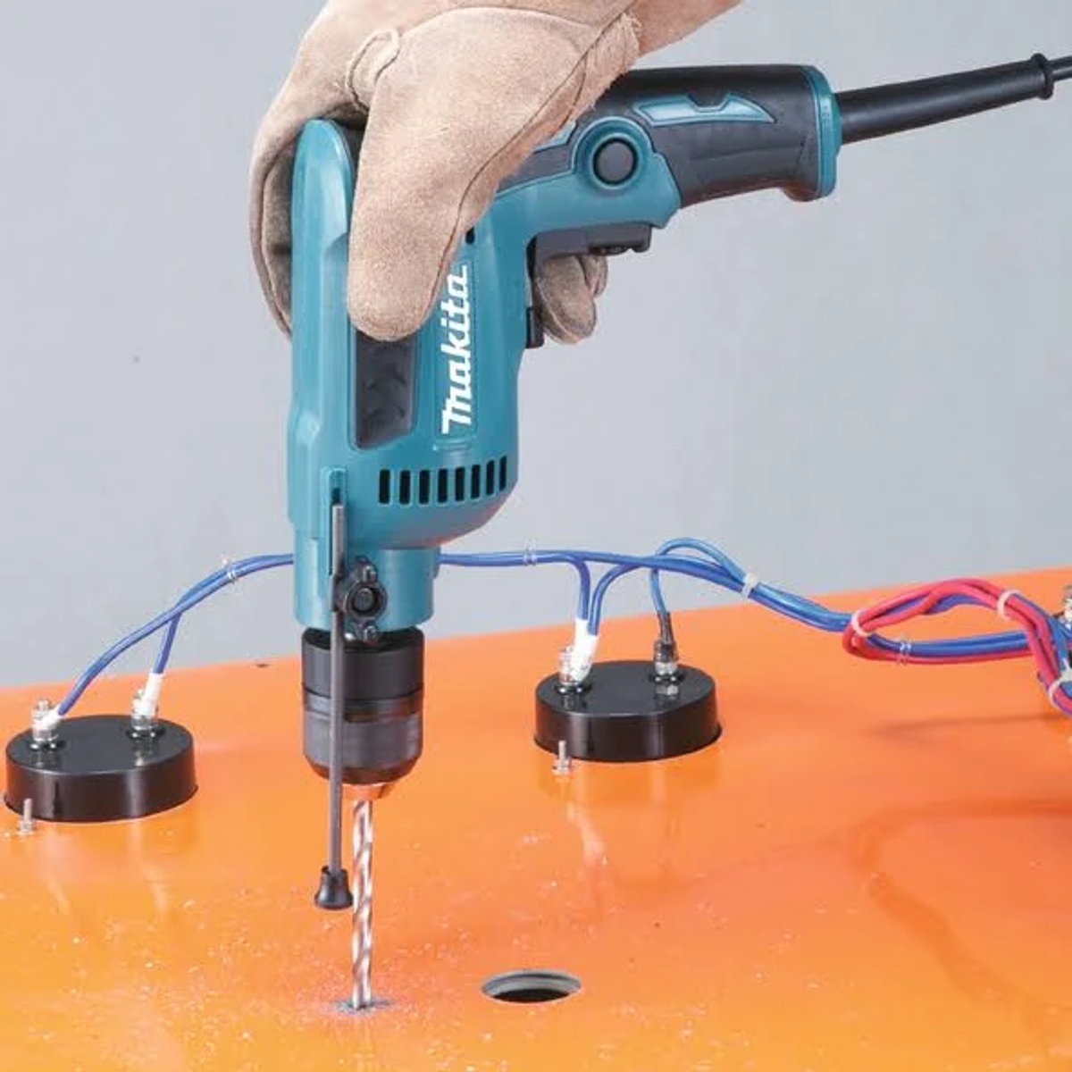 Una persona che fora un foro con un trapano Makita verde acqua in una superficie arancione.